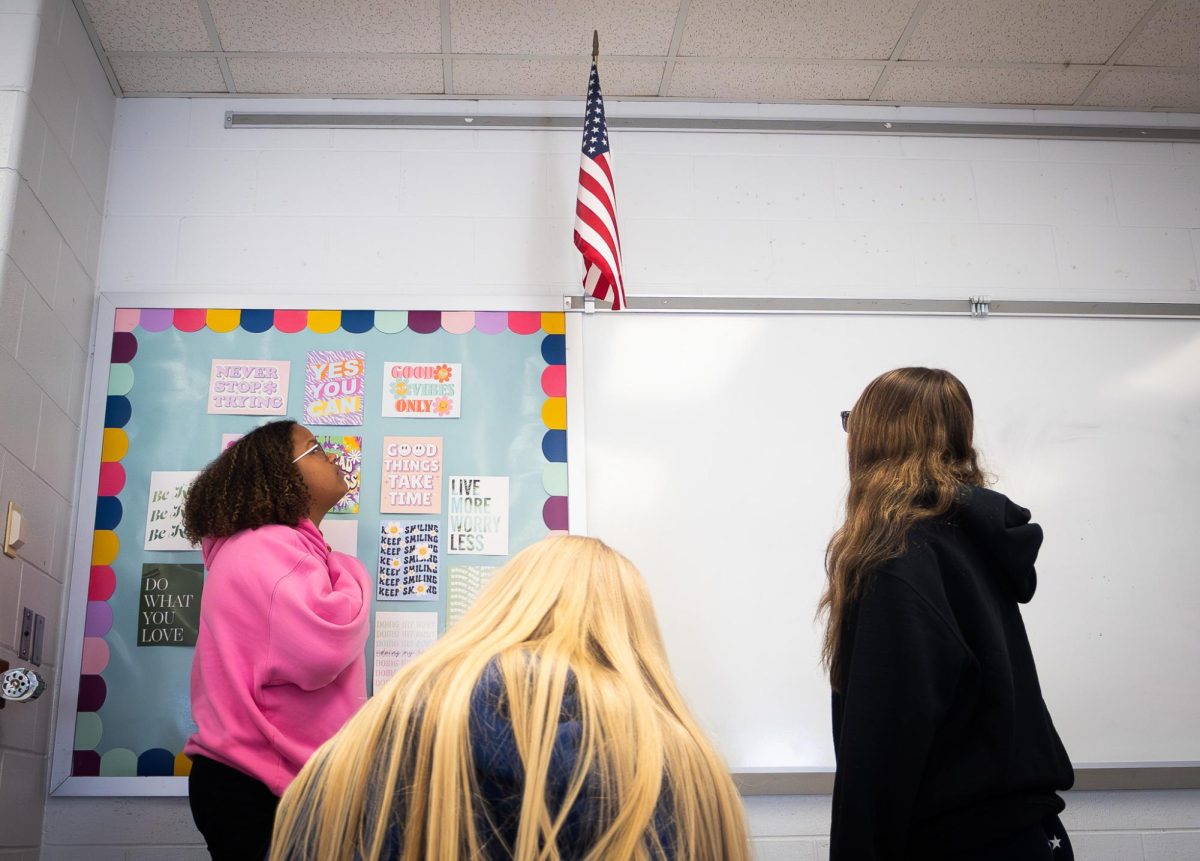 Two onlookers stand for the Pledge of Allegiance while one student abstains from participating in the recitation of the pledge. 