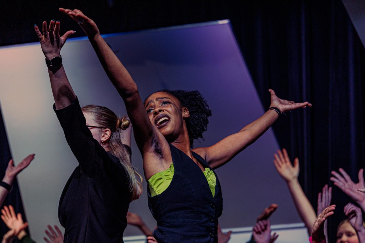 Raising her arms while singing, Mar. 2, senior alto Katelyn Hewing performs during the concert. Hewing joined the Treble Choir only a month before the performance, with a band background, Hewing was able to adapt to the choir setting.