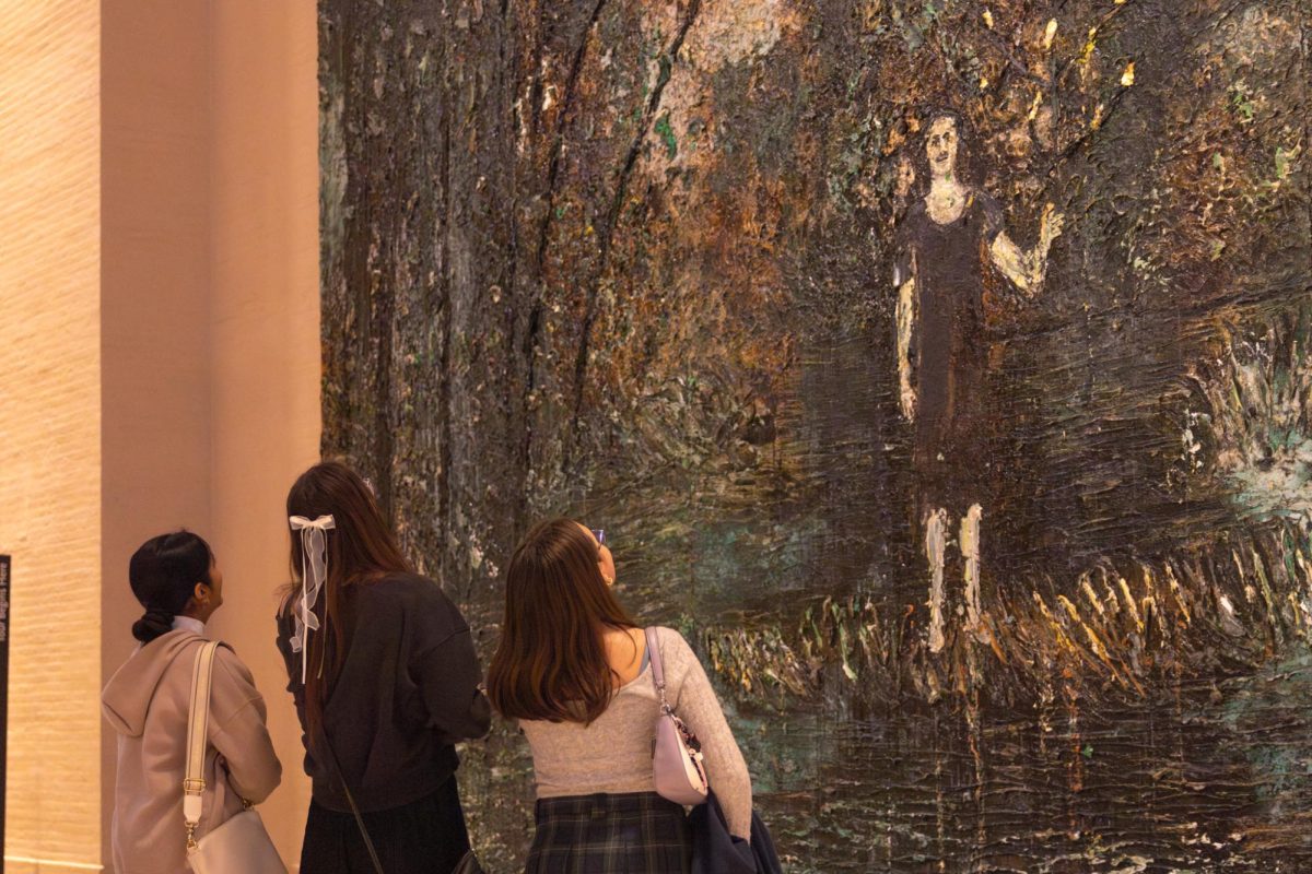 The 30-foot painting, Anselm fuit hic (Anselm Was Here) by Anselm Kiefer, towers above seniors Parneet Chahal, Elaine andert, and Olivia Dalton as they gaze at the woman standing in the forest on March 3. They speculate how the artist could've completed this large painting without using multiple canvases.