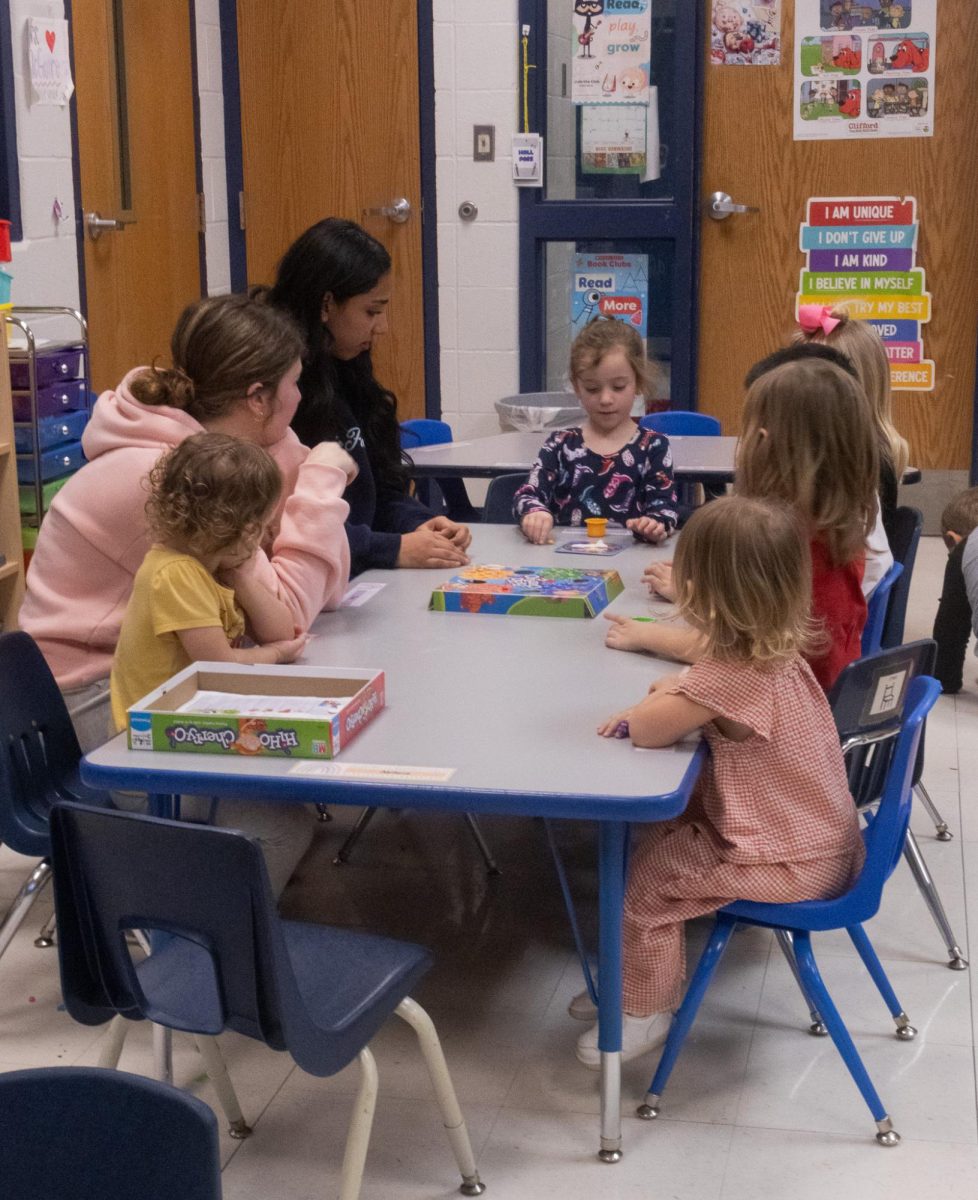 Sitting at the end of the table one little girl talks to her other friends as they take turns playing Hi Ho! Cherry-O. Sophomores Mia Zimmerman and Ayah Elgazar watch the children intently as they play on Feb. 18.