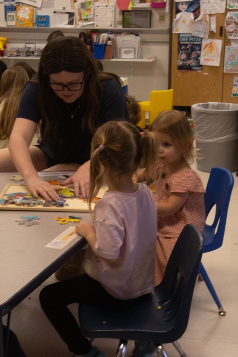 As two little girls quietly work with one another on a puzzle senior Madi Willis steps in to help the little girls on Feb. 18. The girls watch calmly as the teacher moves the pieces around to the correct spots.