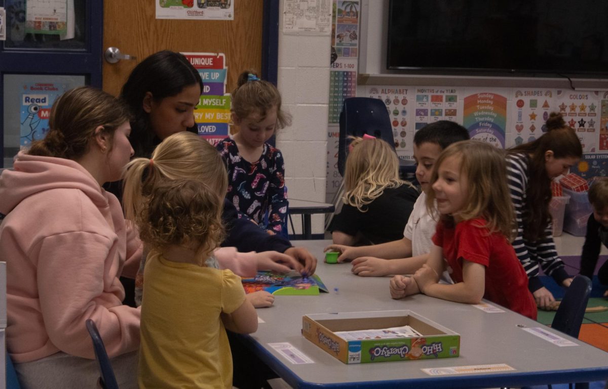 Sitting at the end of the table one little girl talks to her other friends as they take turns playing Hi Ho! Cherry-O. Sophomores Mia Zimmerman and Ayah Elgazar watch the children intently as they play on Feb. 18.
