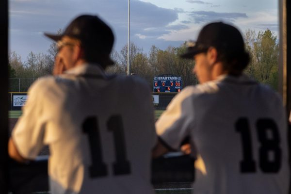Juniors Brody McAllister and Will Brown look toward the field as their team takes the field late in the game on April 9. The scoreboard, though in the sixth inning, reflects the final score after seven innings. 