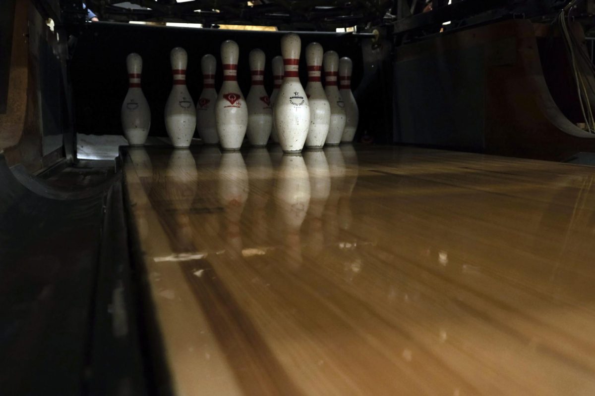 A formation of pins stands at the end of the bowling lane. The pin setter machine sets the pins the exact same every time, but if a pin is slightly moved when a ball hits it, the machine keeps the integrity of the pin, not setting it perfectly back to its original position.