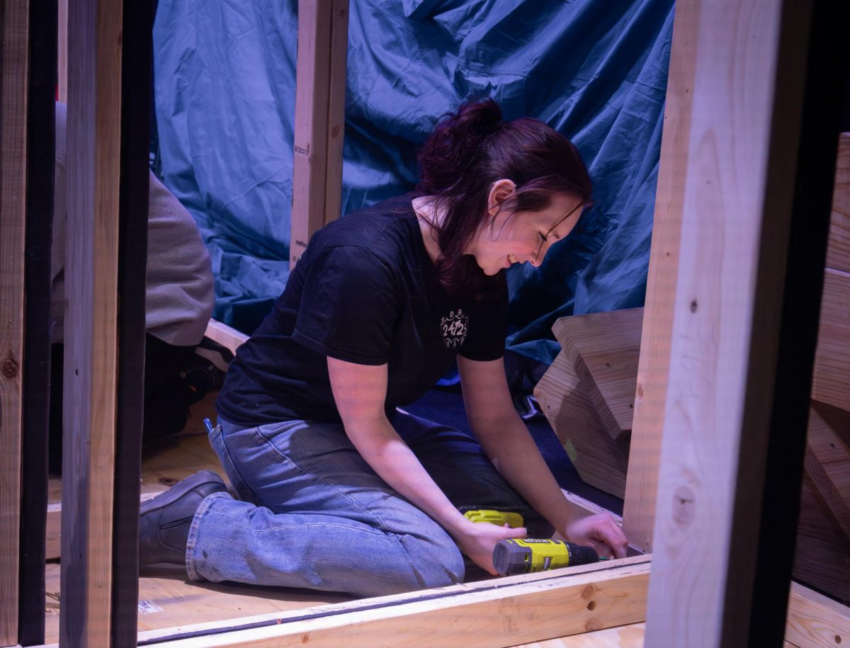Laughing at a statement another member said, Lyra Hobson drills a nail to secure a beam on Feb. 23. As paint crew leader, Hobson and her crew also work on building the set.