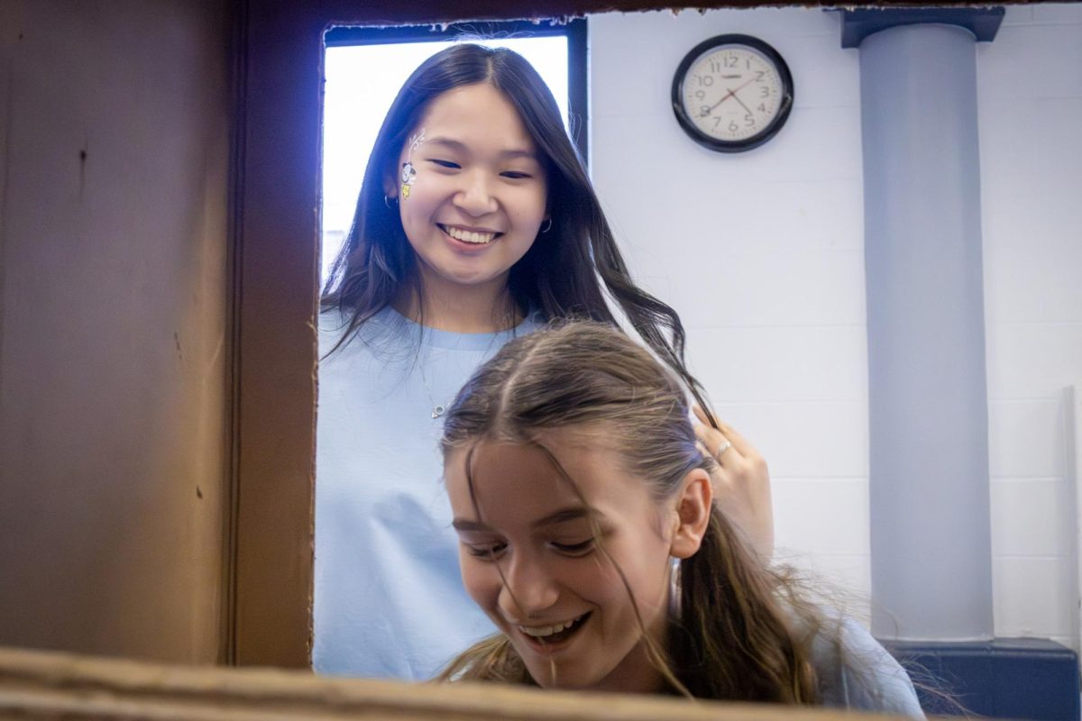Juniors Megan Hoffmann and Megan Chiu laugh together as Hoffmann doodles during her turn as a doodler. During the Fine Arts Festival on March 13, Chiu and Hoffmann take turns doodling at the doodle booth.