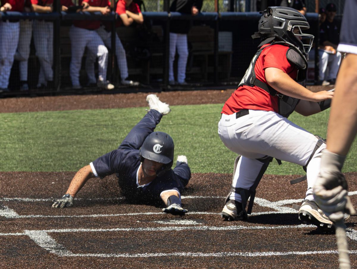 Launching turf into the air with his outstretched hand, Will Brown nears the plate with his dive on April 25. The catcher behind him had just caught the ball, but did not turn around fast enough to get the tag before Brown scored. 