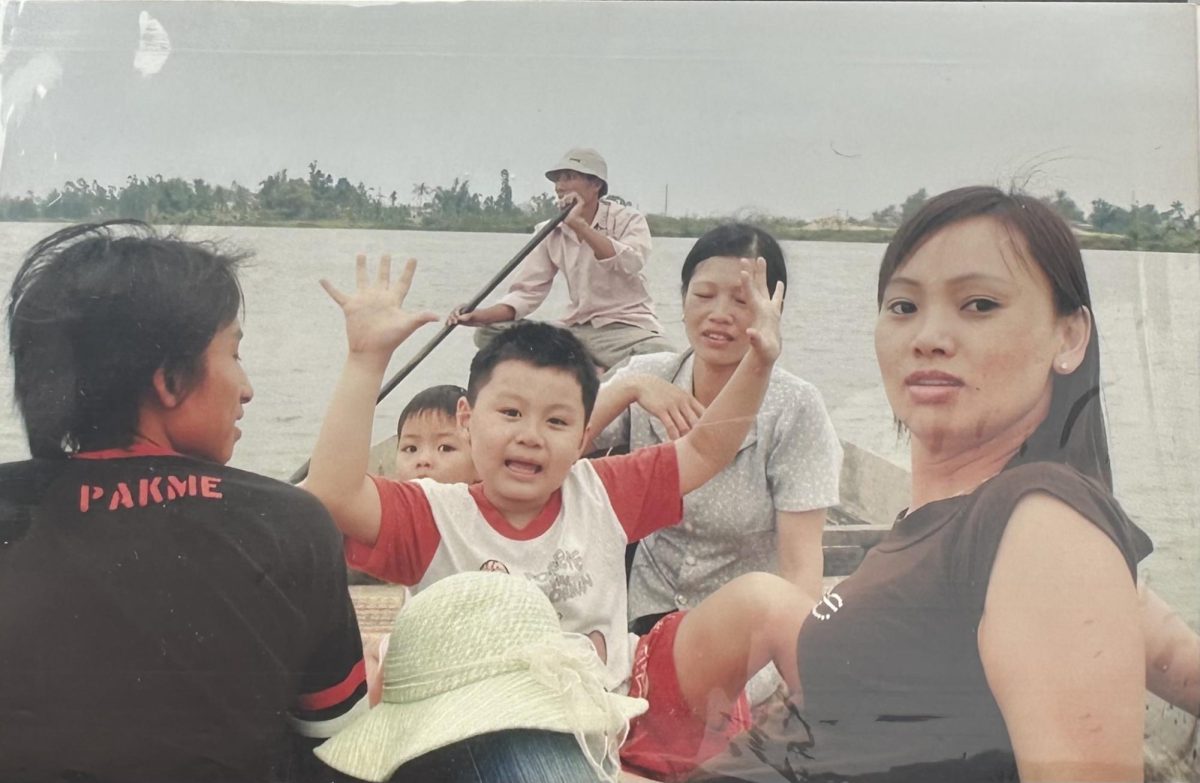 Senior Katie Huynh's family gliding across a lake on a boat. Huynh's brother holds his hands up wide and smiles for the camera, like his mother. 