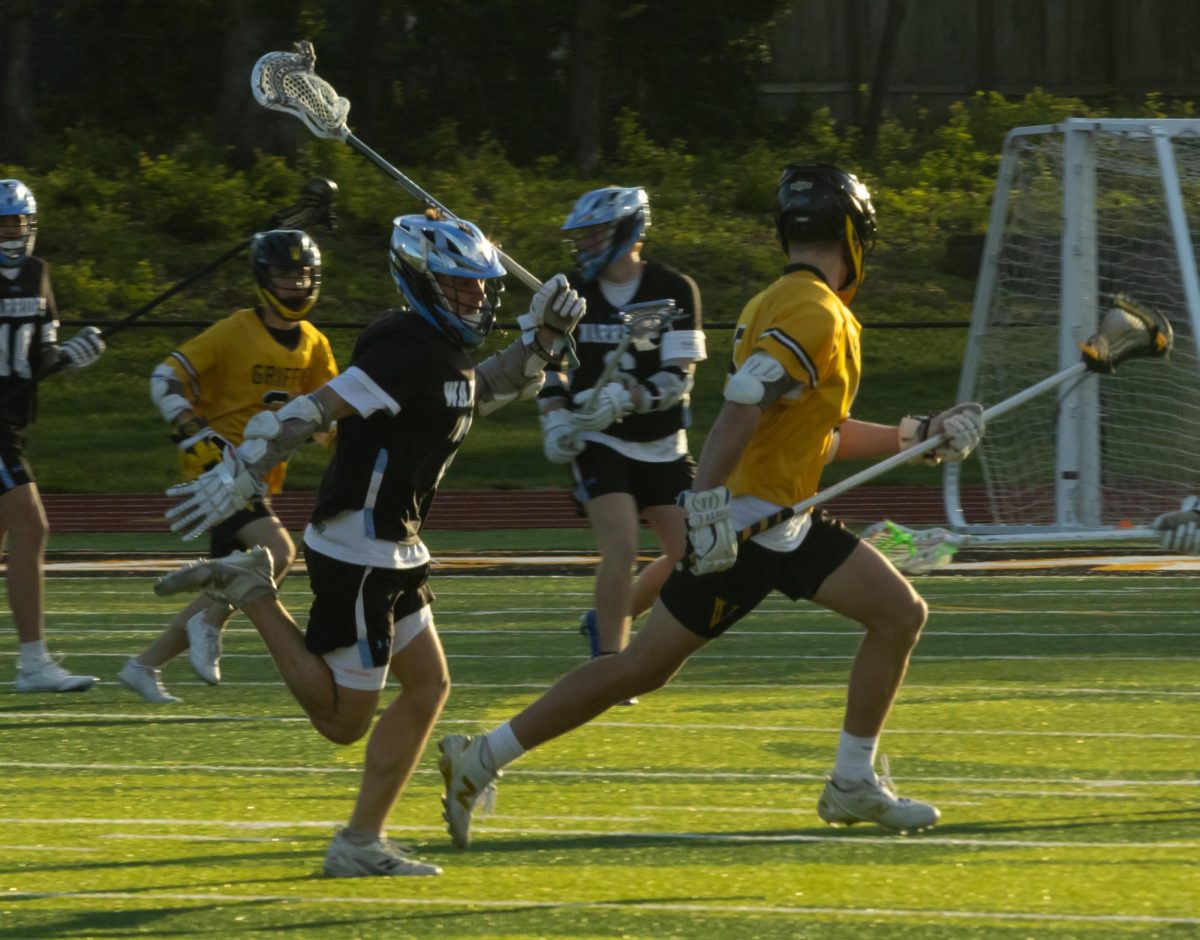 As he runs, senior Brady Dethloff raises up his stick to hit the other player's stick to get the ball back for their team at the game on April 7th. Dethloff checked the player, got the ball back and went to score.