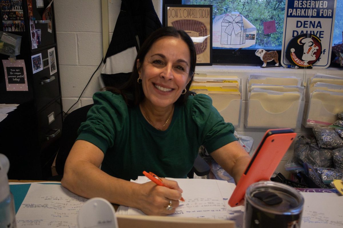 On April 16, Mrs. Dauve poses for a photo in front of the camera. By holding her calculator and planning out her lessons for the week Mrs. Dauve conveys her love for not only her students but her love for them as well. As she plans out her lesson plans for the week, her students are able to not only comprehend her lessons but thrive using the skills they learn.
