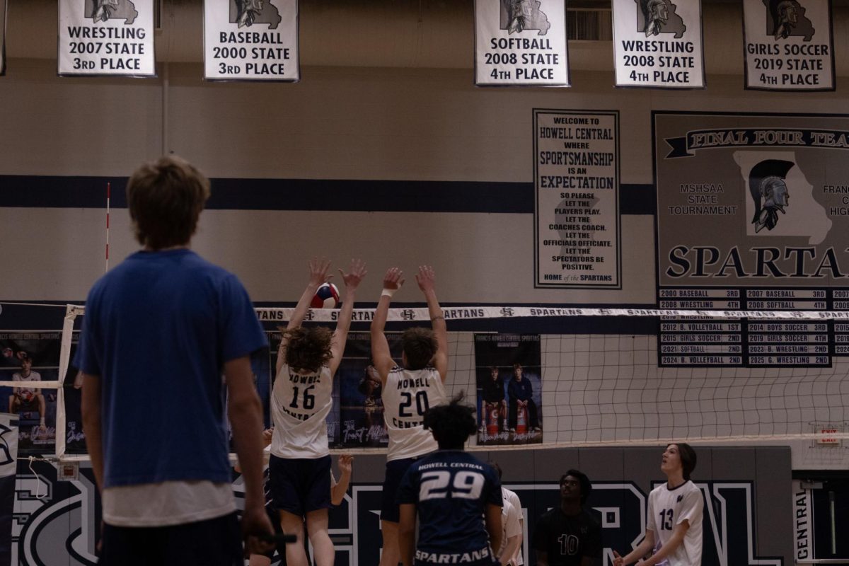 As Kevin Wittig and sophomore Owen Barbeau block the ball from the opposing team, line referee junior Lincoln Buchheit watches during the game on April 23. Varsity players are used as referees for the JV matches to call balls close to the line.