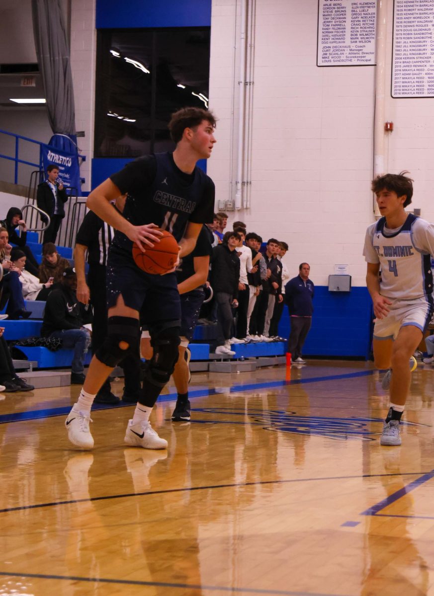 Senior Wyat Dwyer prepares to pass the ball. Behind him, a player from St. Dominic's High School catches up to block. 