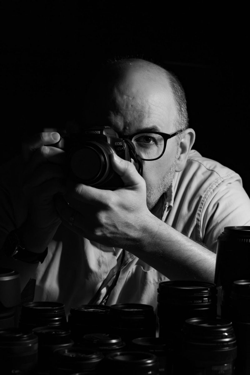 Selecting his lens of choice, Matthew Schott places his eye through the viewfinder searching for a subject on April. 20. Schott has been working at the school for 21 years.