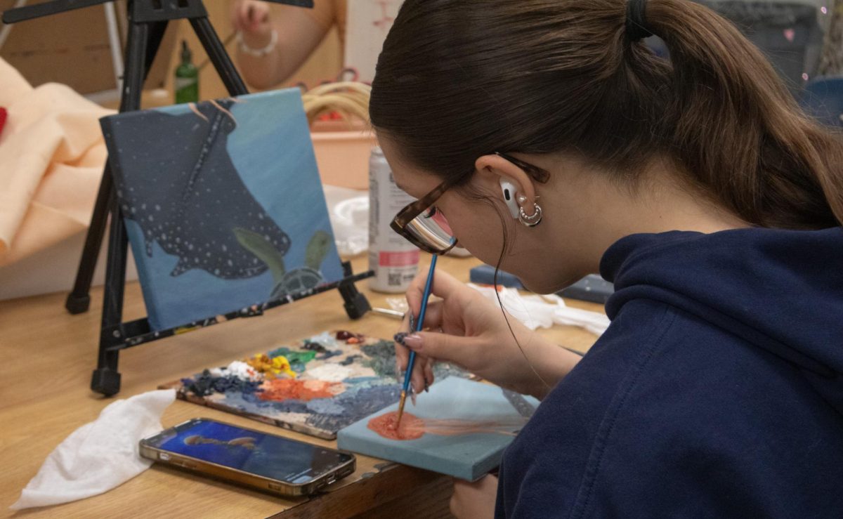 Senior Kalynn Bilodeau listens to her music as she adds the final touches to her jellyfish on April 30. Her three canvases fit together as a scene of ocean creatures swimming together, and as she is almost finished with one, she prepares to add the final touches to another.
